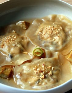 a white bowl filled with dumplings covered in sauce and toppings on top of a wooden table