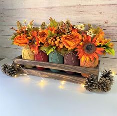 an arrangement of sunflowers and pine cones in mason jars on a wooden stand