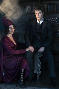 a man and woman sitting on a chair in front of a book shelf