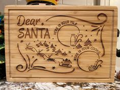 a wooden cutting board with the words dear santa written in black on it, and a christmas tree behind it