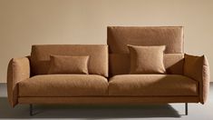 a brown couch with pillows on it in front of a beige wall and grey floor