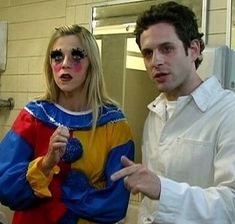 a man and woman dressed up as clowns in a bathroom with one pointing at the mirror