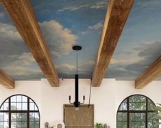 a living room filled with lots of furniture under a painting on the ceiling and two large windows