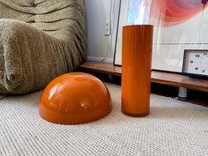 an orange vase sitting on the floor next to a brown chair and a tan blanket