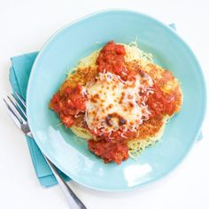 a blue plate topped with spaghetti and sauce on top of a white table next to silverware