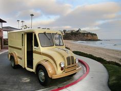 an old yellow truck is parked on the side of the road by the beach and ocean