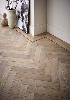 a vase with flowers on the floor next to a wooden herringbone pattern wallpaper