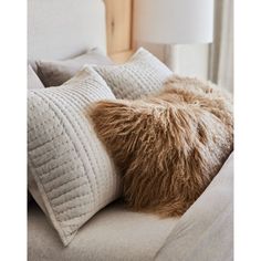 a close up of pillows on a couch with a lamp in the backgrouund