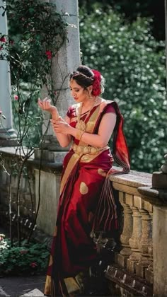 a woman in a red and gold sari looking at her cell phone while sitting on a stone wall