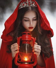 a woman dressed in red holding a lantern with a light on it's face