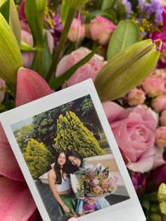 a person holding up a polaroid photo with flowers in the back ground behind them