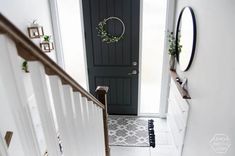 a black door with a wreath hanging on it's side next to a white stair case