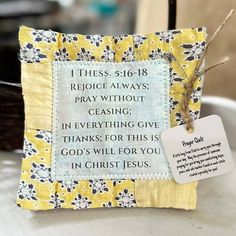 a small yellow and white pillow with a bible verse on it's front, sitting on a table