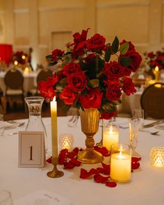 red roses in a gold vase on a table with candles and rose petals around it