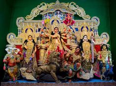 an elaborately decorated stage with statues and people on it's sides, in front of a green wall