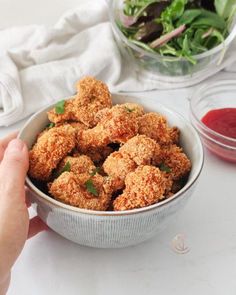 a person holding a bowl full of fried food next to salad and ketchup