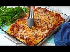 someone is using a spatula to mix ingredients in a casserole dish with parsley on the side