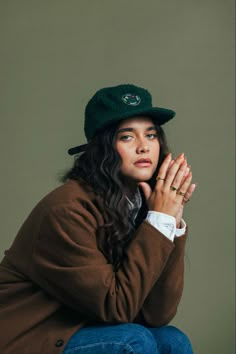 a woman sitting on the ground wearing a hat and holding her hands to her chest