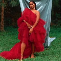 a woman in a red dress standing next to a blue backdrop with trees and grass