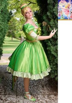 a woman in a green dress is posing for the camera with her hands out and trees behind her