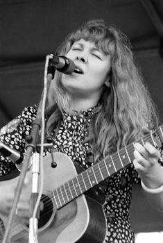 a woman singing into a microphone while holding a guitar