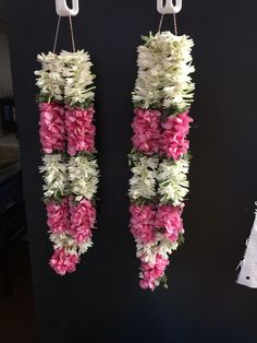 two white and pink flowers hanging from hooks on a black wall next to each other