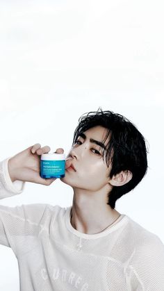 a young man is drinking from a blue cup while wearing a white sweater and black hair