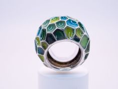 A gorgeous enameled ring in a size 7 1/2. Featuring a beautiful selection of blue and green enamel colors with a lovely emerald hidden on the back of the ring for the wearer to admire. This sculptural ring wears very comfortably and will bring a splash of bright color and joy to any day; sure to pair well with any outfit. Materials: Glass Enamel, Natural Emerald, Sterling Silver Enamel Fine Jewelry, Elegant Green Enamel Ring, Green Enamel Round Ring, Modern Green Round Dome Ring, Green Enamel Rings As A Gift, Unique Blue Enamel Ring, Unique Green Open Ring, Green Handmade Fusion Rings, Unique Green Enamel Ring For Gift