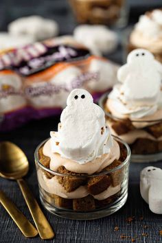 two small glass dishes with marshmallows and ghost faces on them, next to gold spoons