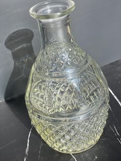 a clear glass vase sitting on top of a black marble table next to a gray wall