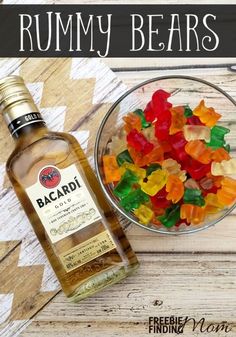 a glass bowl filled with gummy bears next to a bottle of alcohol on top of a wooden table