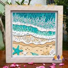 a picture frame that has some sand and sea shells on it with pink flowers in the foreground