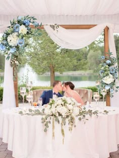 a bride and groom kissing in front of a table with flowers on it at their wedding reception