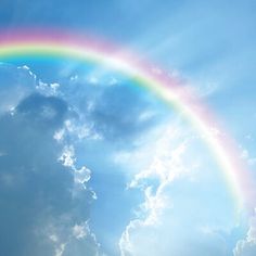 a rainbow in the sky with clouds and blue sky behind it that is partially obscured by sunbeams