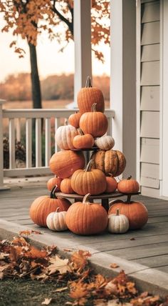 a stack of pumpkins sitting on top of a wooden porch next to a tree