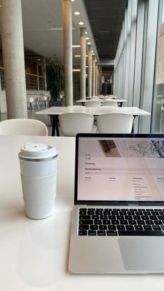 an open laptop computer sitting on top of a white table next to a cup of coffee