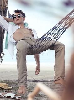 a man sitting in a hammock on the beach with his feet propped up