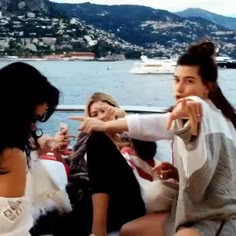 three women sitting on a boat in front of the water, one pointing at something