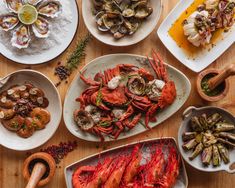 lobsters, clams and other seafood are served on white plates with wooden serving utensils