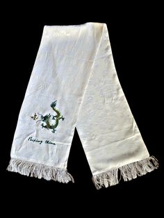 This ivory floral embossed novelty scarf features a green embroidered dragon, perfect for 2024. Peiping China embroidered underneath. 2" fringe accent on ends. I'm unsure of the material. Poly? Rayon? Its silky but I'm not sure its silk.  Vintage condition excellent Traditional White Embroidered Scarves, Luxury Elegant Embroidered Scarf, Elegant White Embroidered Scarf, Elegant Floral Embroidered Shawl Scarves, White Bohemian Embroidered Scarf, Embroidered Scarf, Scarf Wrap, Scarf Accessory, Etsy Accessories