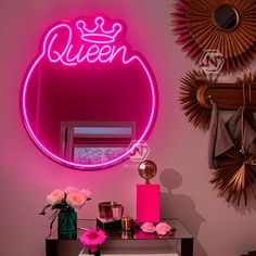 a pink neon sign that says queen on it next to a mirror and vase with flowers