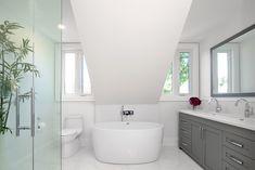 a large white bath tub sitting next to a toilet under two windows in a bathroom