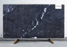 a large black marble slab sitting on top of a wooden stand in front of a white brick wall