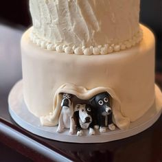 a three tiered cake with white frosting and two black dogs on the side