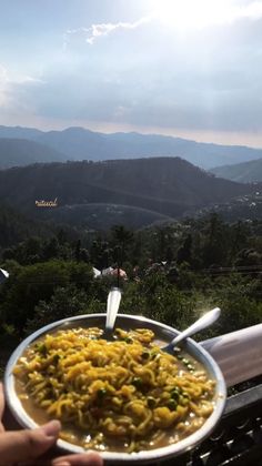 a person holding a bowl of food with mountains in the background