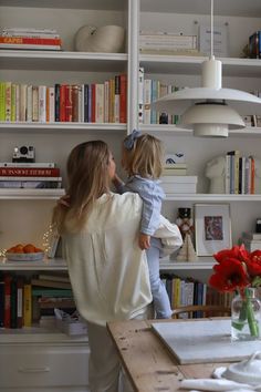 a woman holding a child in her arms near a book shelf with books on it