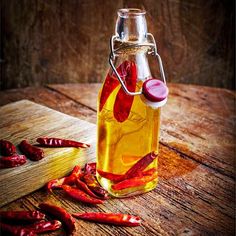 a glass bottle filled with hot sauce sitting on top of a wooden table next to red peppers