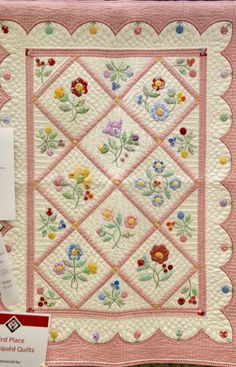 a pink quilt with flowers on it next to a card and some other sewing supplies