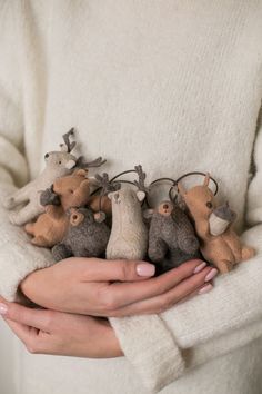 a woman holding several small stuffed animals in her hands, all wearing reindeer antlers