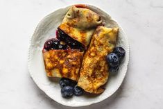 blueberry crepes on a white plate topped with fresh berries and orange slices